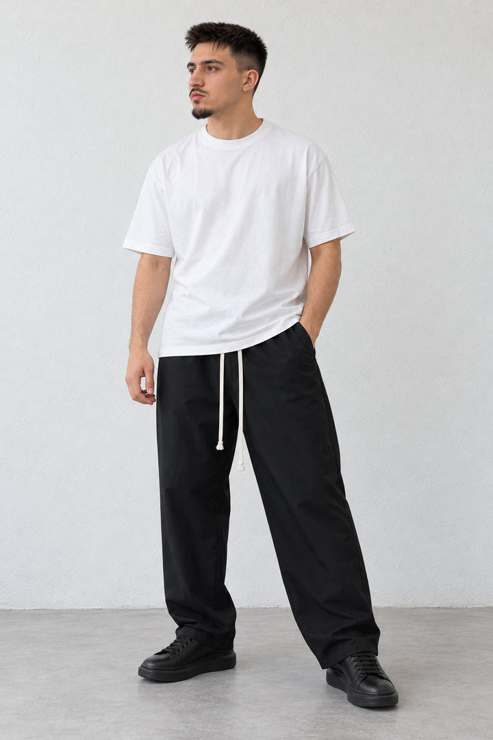 Pantaloni negri lejeri cu șnur ivoriu lung, combinați cu tricou alb, modelul orientat spre stânga.