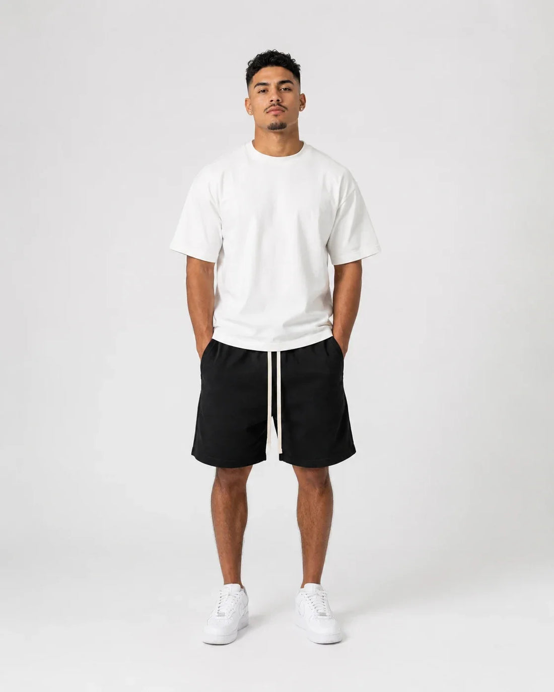 Bărbat în tricou alb, pantaloni scurți negri cu două șnururi deschise și sneakers albi