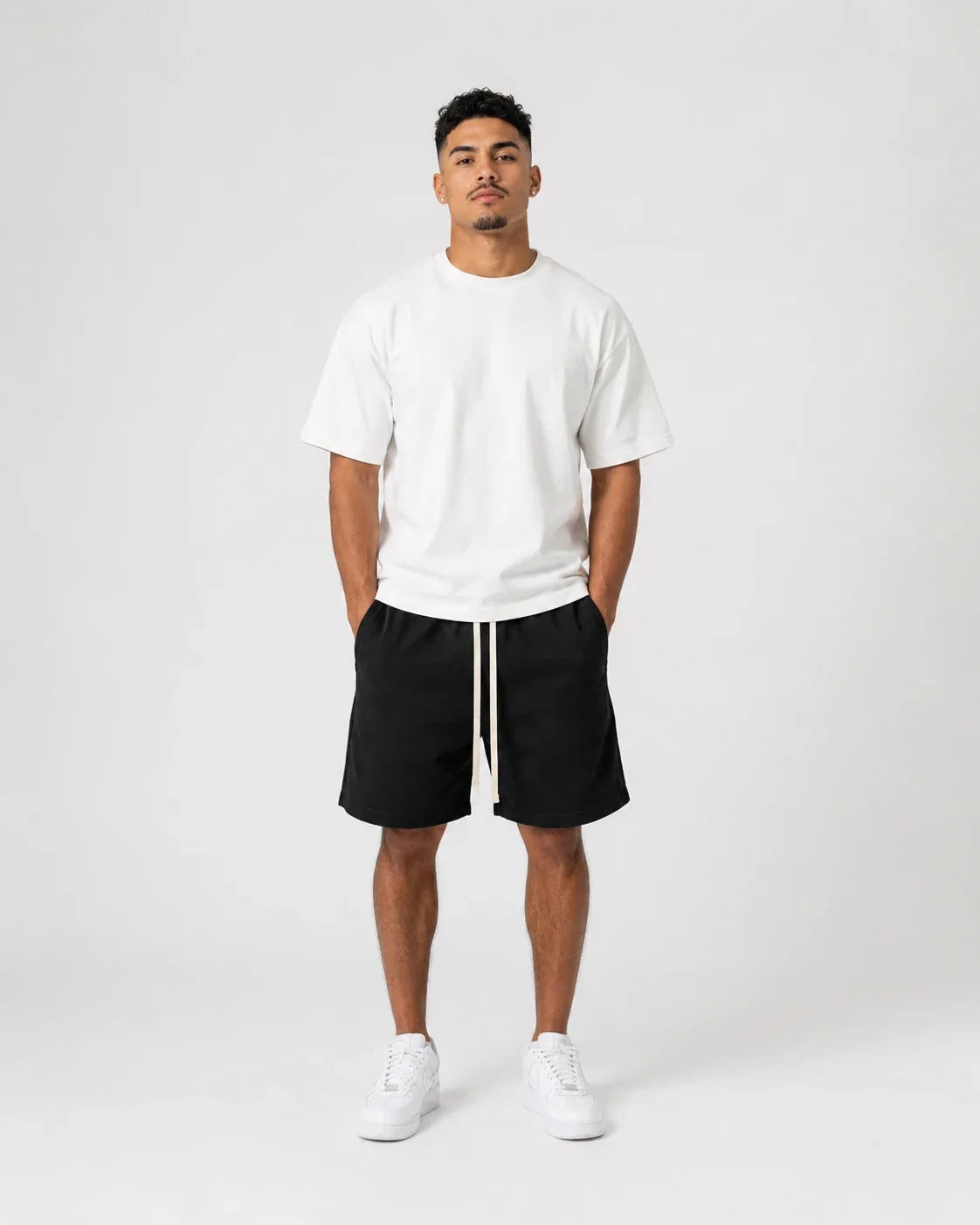 Bărbat în tricou alb, pantaloni scurți negri cu două șnururi deschise și sneakers albi
