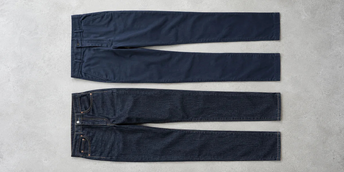 Pantaloni chino bleumarin și blugi indigo, întregi, așezați orizontal pe o suprafață gri