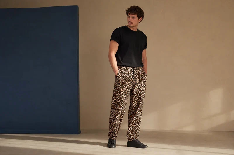 Bărbat cu tricou negru și pantaloni cu imprimeu leopard, pe fundal bej și albastru