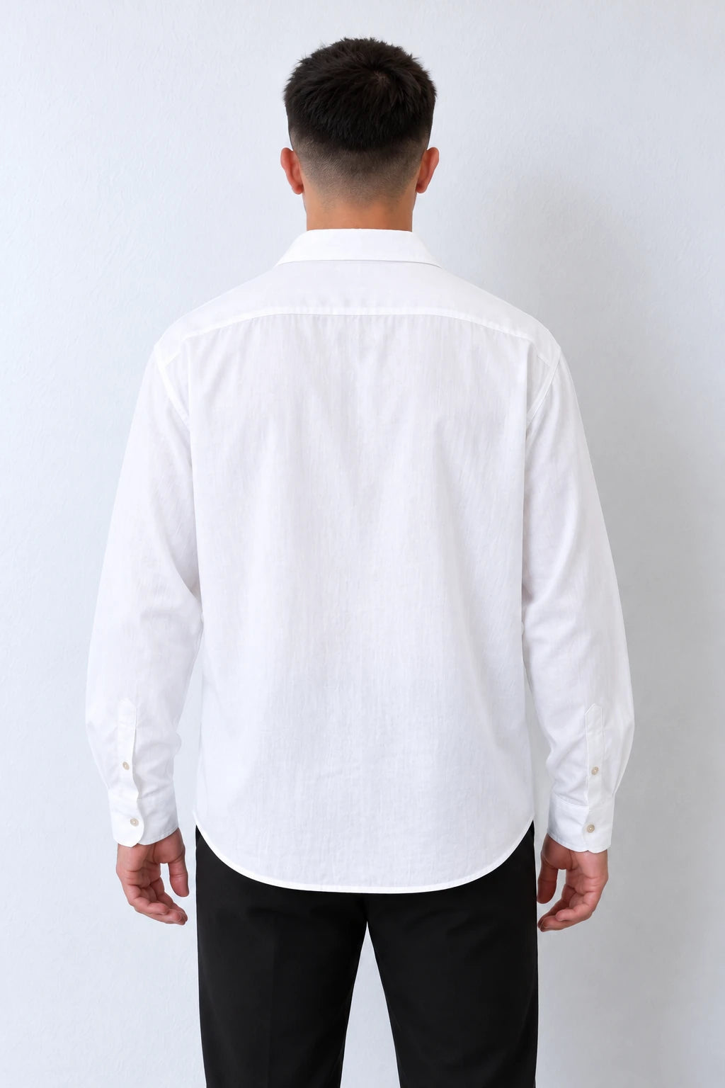 Cămașă albă oversized pentru bărbați, vedere din spate pe model, cu mâneci lungi și tiv rotunjit.