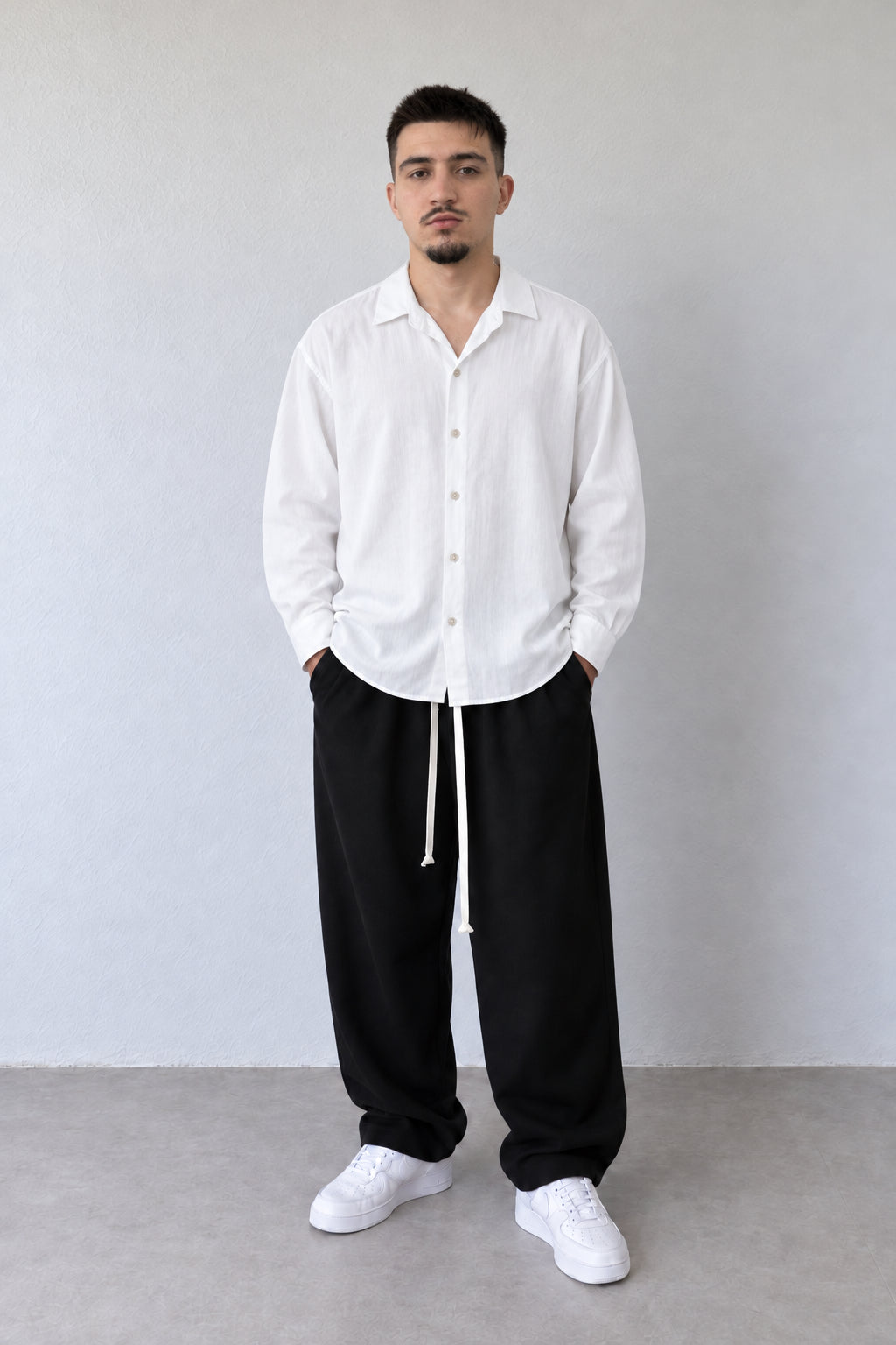 Cămașă albă oversized pentru bărbați din vâscoză și in, purtată lejer peste pantaloni negri largi cu șnur lung.