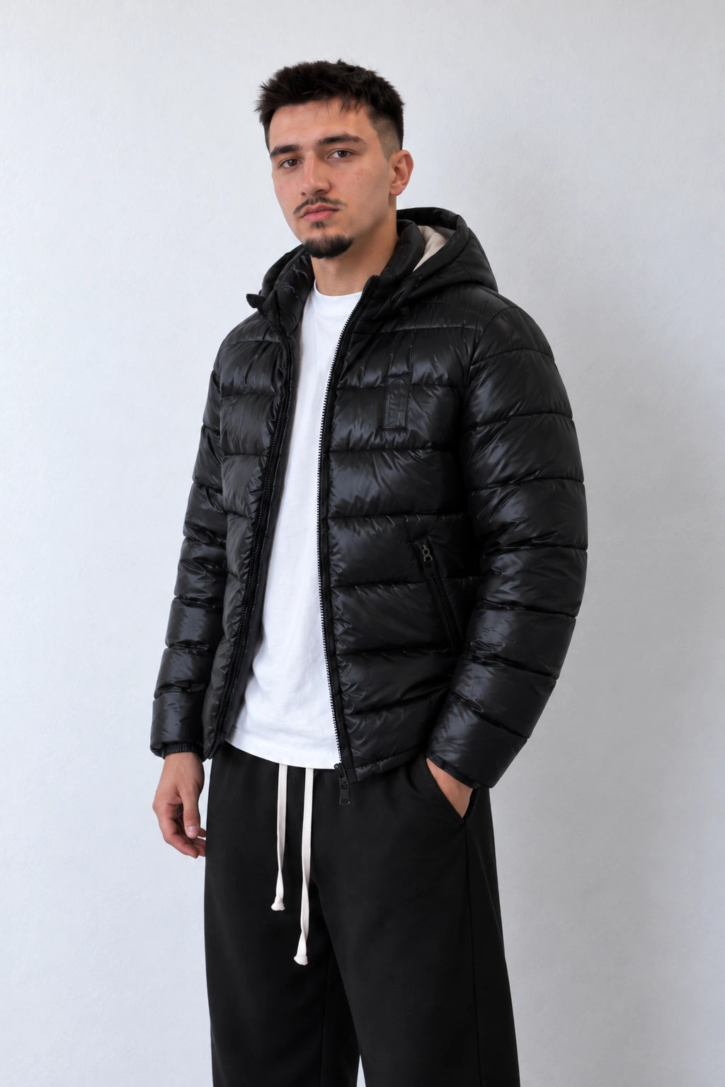 Geacă puffer neagră cu glugă și matlasare orizontală pentru bărbați, vedere din trei sferturi pe model.