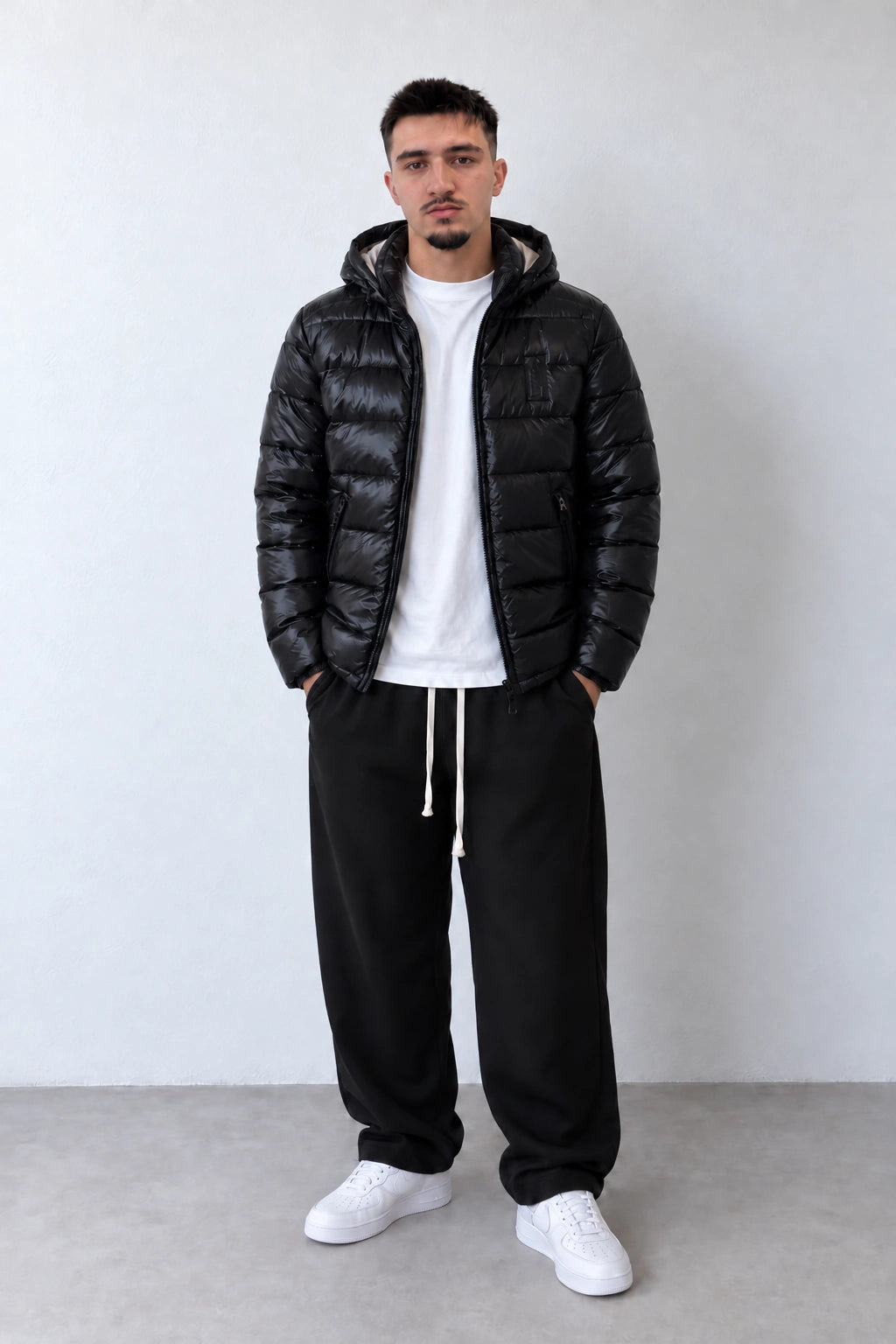 Geacă puffer neagră cu glugă pentru bărbați, purtată deschisă cu tricou alb și pantaloni negri, vedere integrală pe model.