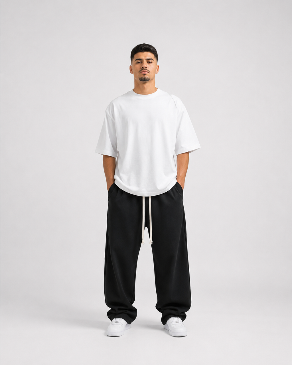 Model masculin purtând pantaloni negri wide leg oversized cu șnur lung și tricou alb oversized premium, aesthetic luxury streetwear minimalist.