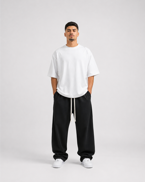 Model masculin purtând pantaloni negri wide leg oversized cu șnur lung și tricou alb oversized premium, aesthetic luxury streetwear minimalist.