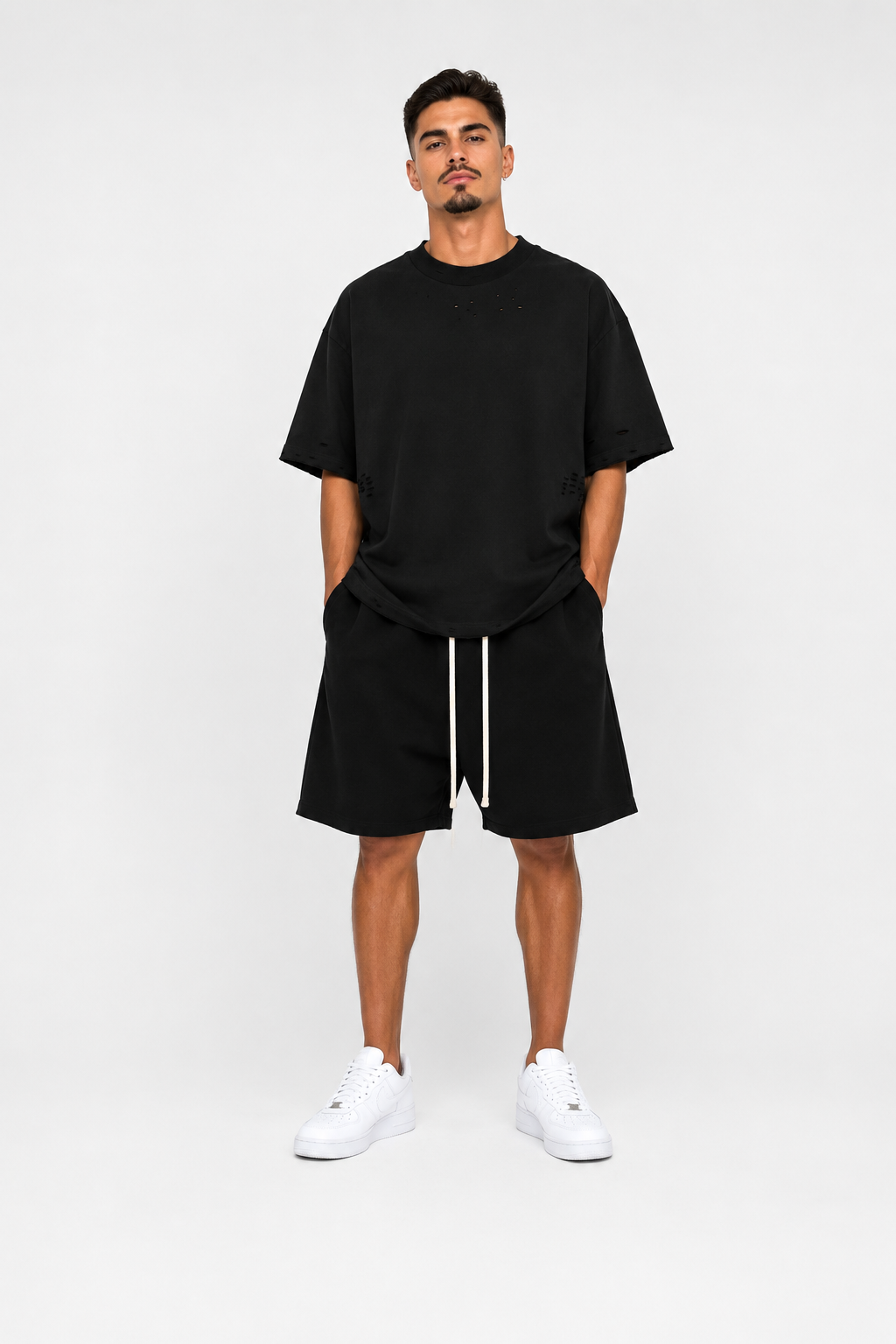 Model masculin purtând tricou oversized negru premium și pantaloni scurți baggy streetwear într-un studio minimalist