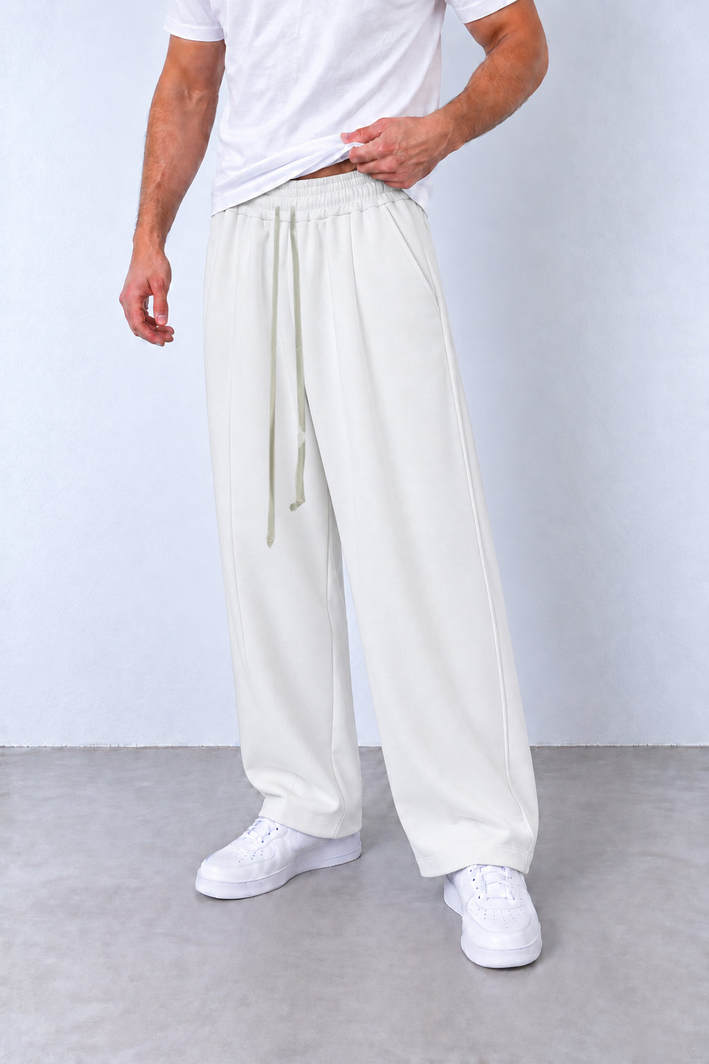 Pantaloni albi LEO26 pe model, vedere din trei sferturi cu talie elastică, șnur lung și tivuri simple.