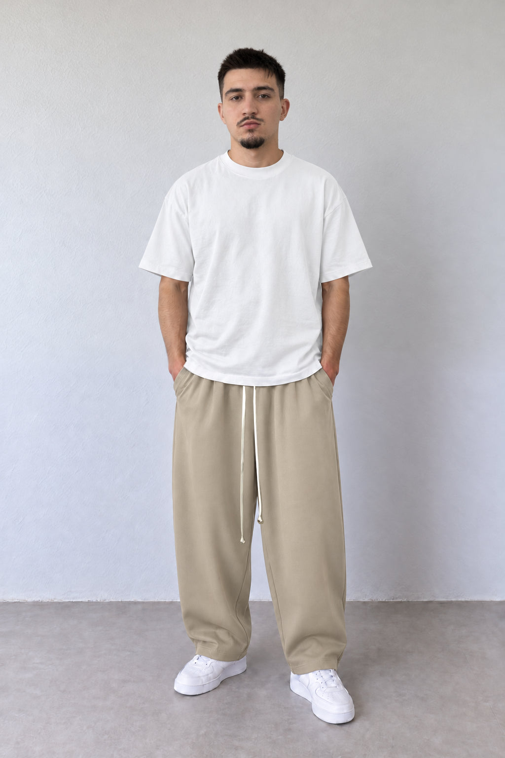Pantaloni baggy bej pentru bărbați, vedere frontală pe model cu tricou alb și șnur lung
