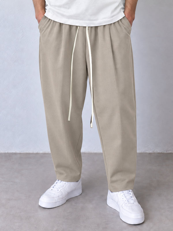 Pantaloni carrot bej, cadru frontal apropiat cu șnur lung și crac îngustat spre gleznă.