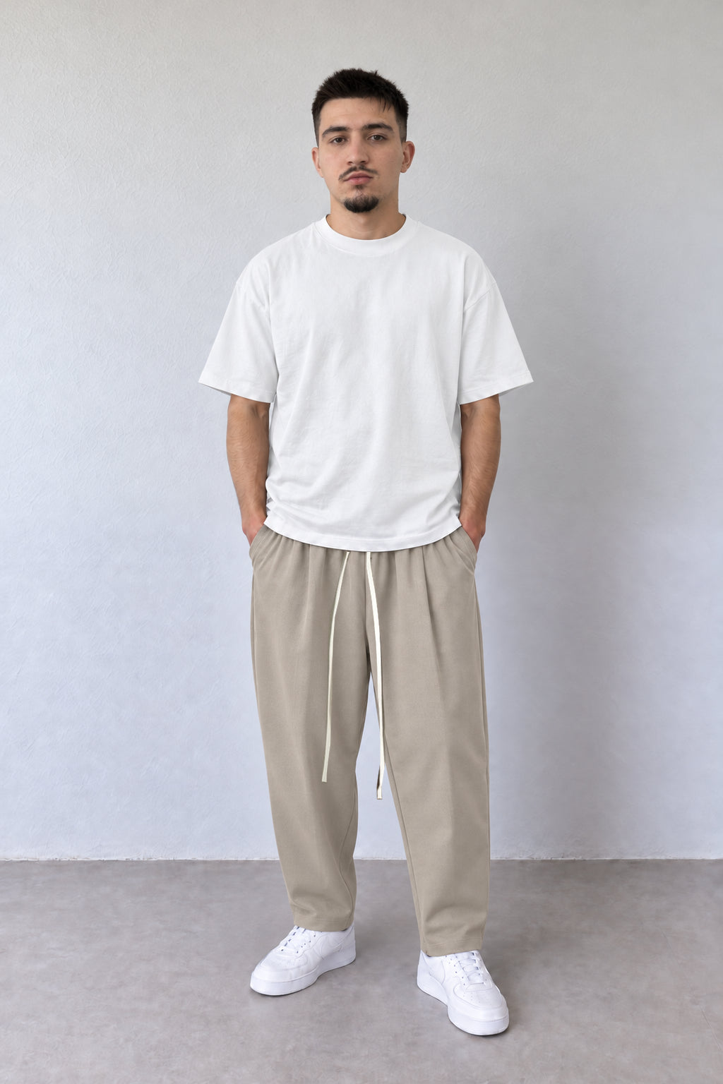 Pantaloni bej carrot fit pentru bărbați, cu șnur lung, purtați cu tricou alb, vedere integrală.
