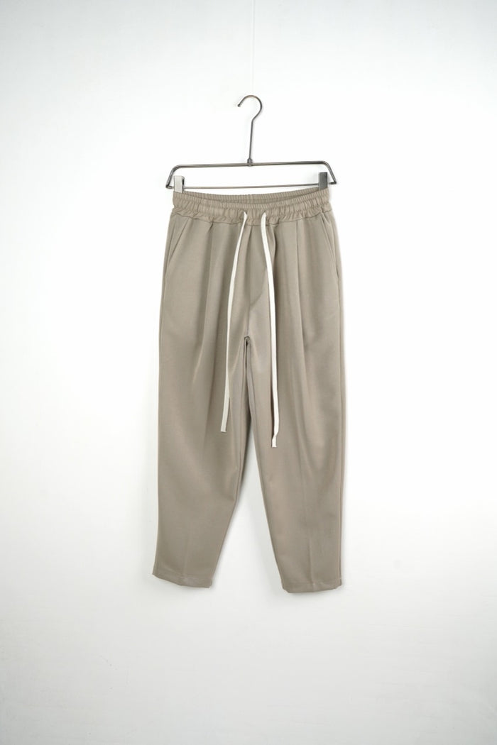 Pantaloni bej carrot fit pentru bărbați, cu talie elastică și șnururi albe, vedere frontală integrală pe umeraș