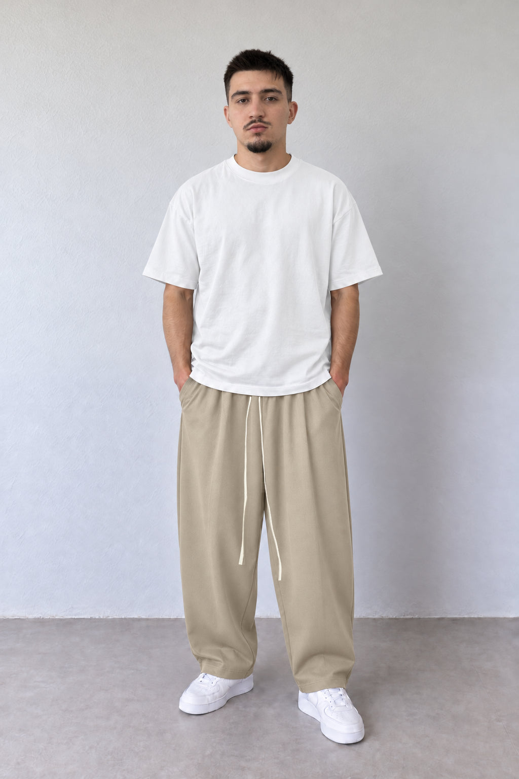 Pantaloni bej baggy pentru bărbați cu șnur alb lung, purtați cu tricou alb, vedere integrală.