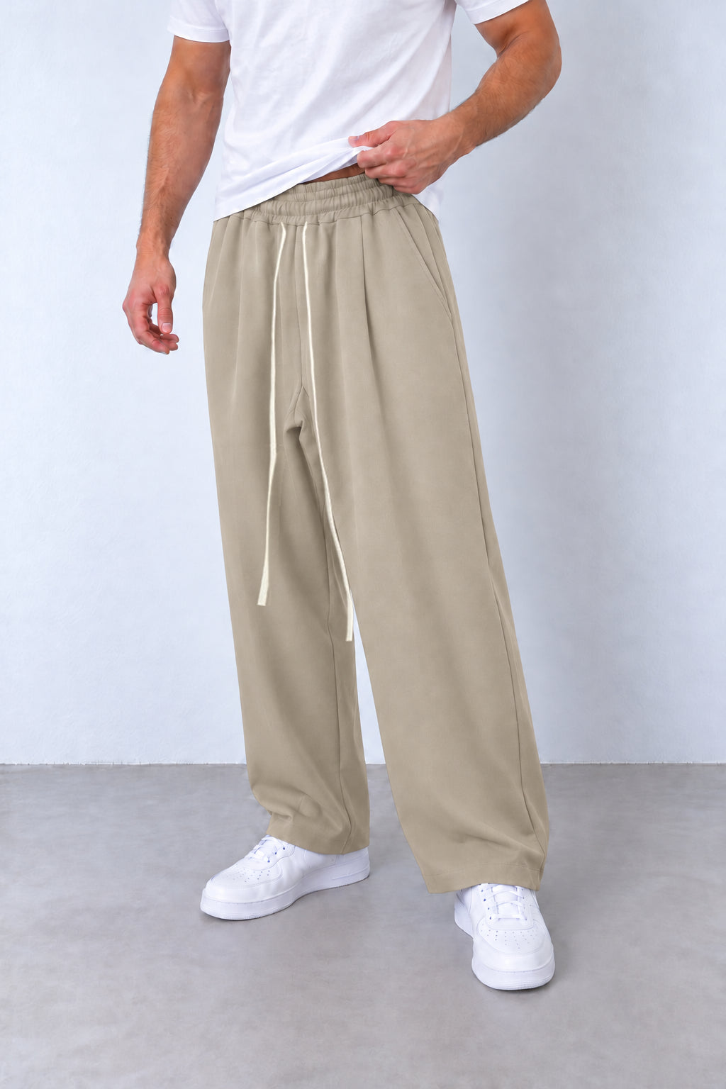 Pantaloni baggy bej pe model, cadru din trei sferturi cu talie elastică și șnur lung.