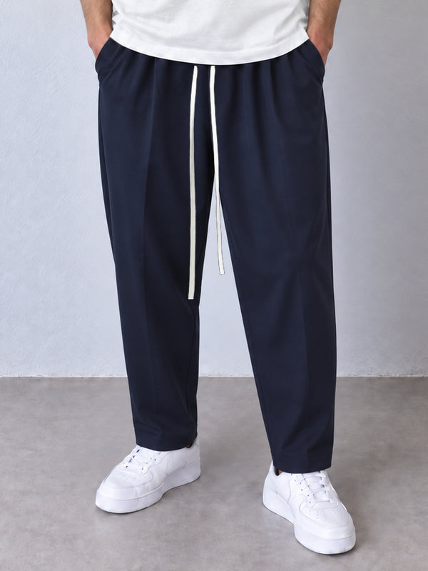 Pantaloni carrot bleumarin, cadru frontal apropiat cu șnur lung și crac îngustat spre gleznă.