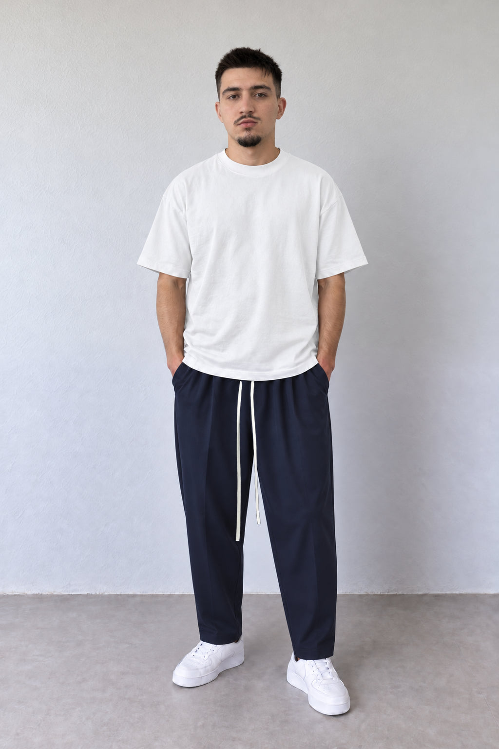 Pantaloni bleumarin carrot fit pentru bărbați, cu șnur lung, purtați cu tricou alb, vedere integrală.
