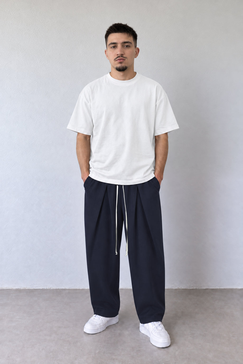 Pantaloni bleumarin pentru bărbați cu pense și șnur lung, purtați cu tricou alb, vedere integrală.