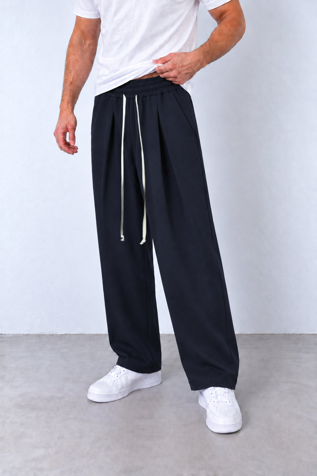 Pantaloni bleumarin cu pense pe model, vedere din trei sferturi cu talie elastică și șnur lung.