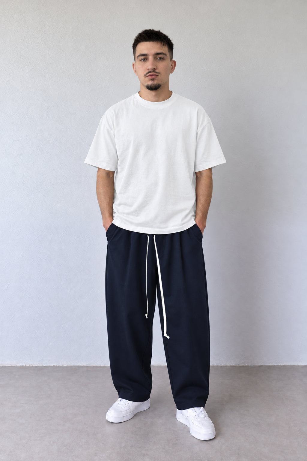 Pantaloni bleumarin pentru bărbați cu șnur alb lung, purtați cu tricou alb, vedere integrală.