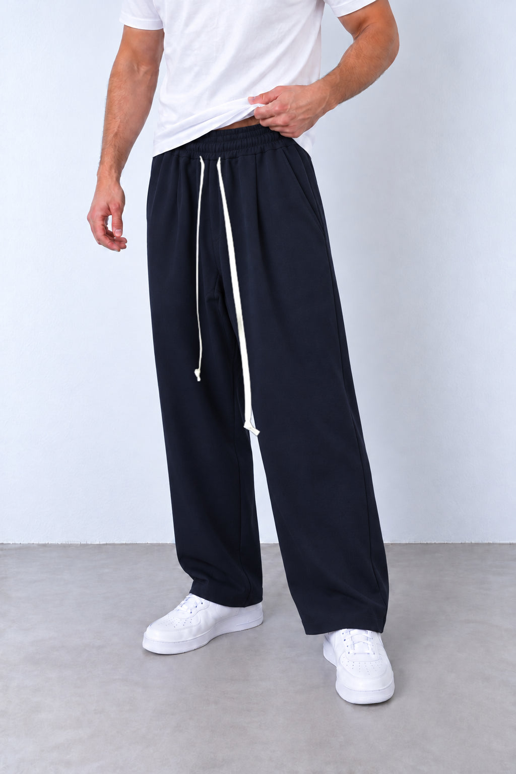 Pantaloni bleumarin pe model, vedere din trei sferturi cu talie elastică și șnur alb lung.