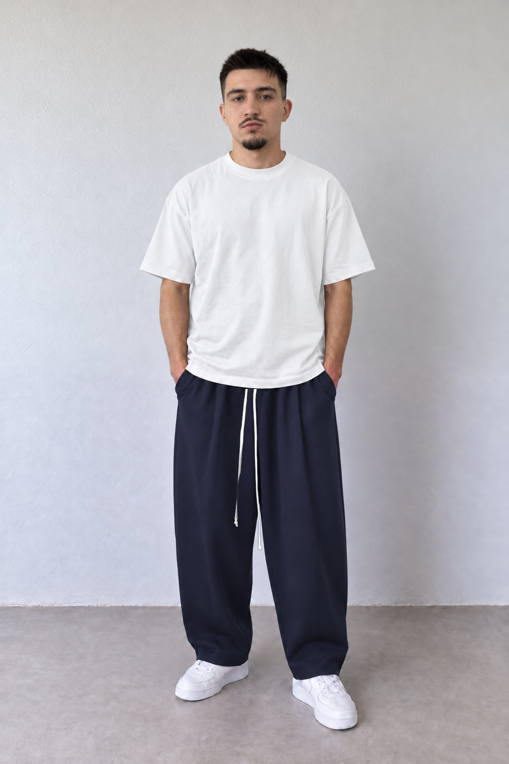 Pantaloni bleumarin baggy pentru bărbați cu șnur alb lung, purtați cu tricou alb, vedere integrală.