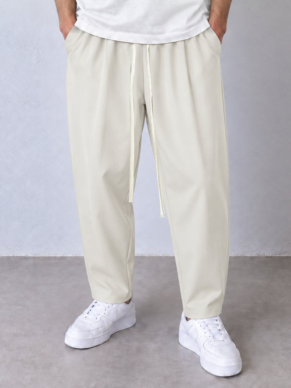 Pantaloni carrot crem, cadru frontal apropiat cu șnur lung și crac îngustat spre gleznă.