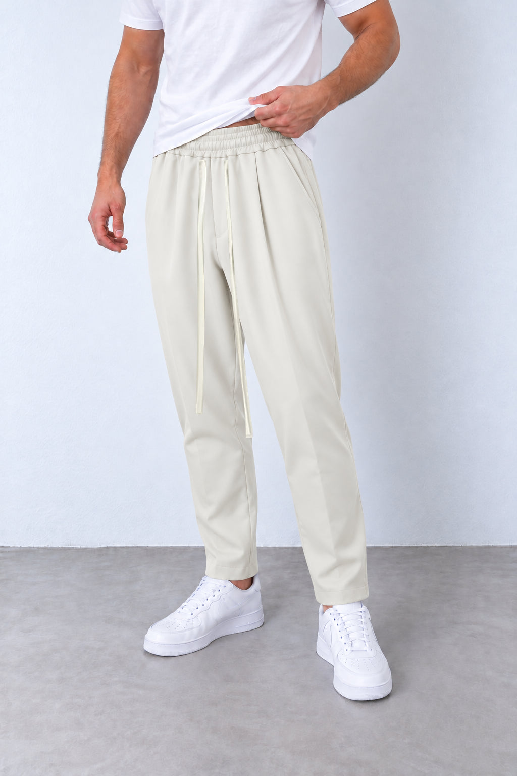 Pantaloni crem pe model, vedere din trei sferturi cu talie elastică și șnur lung.