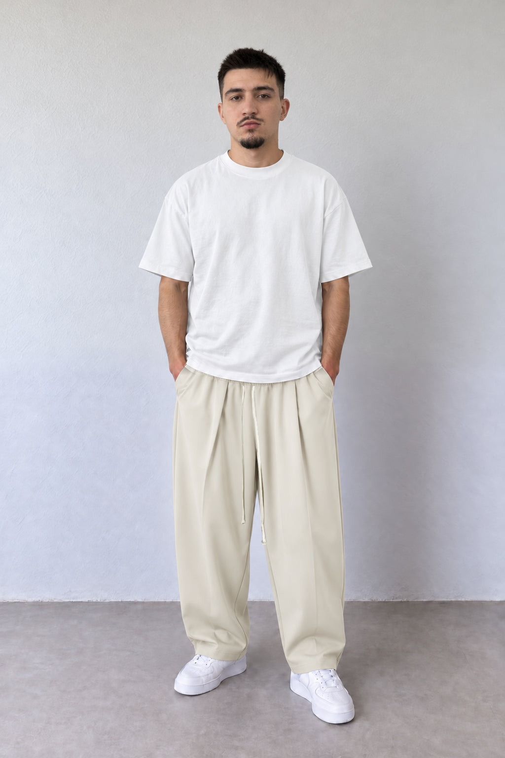 Pantaloni crem pentru bărbați cu pense și șnur lung, purtați cu tricou alb, vedere integrală.