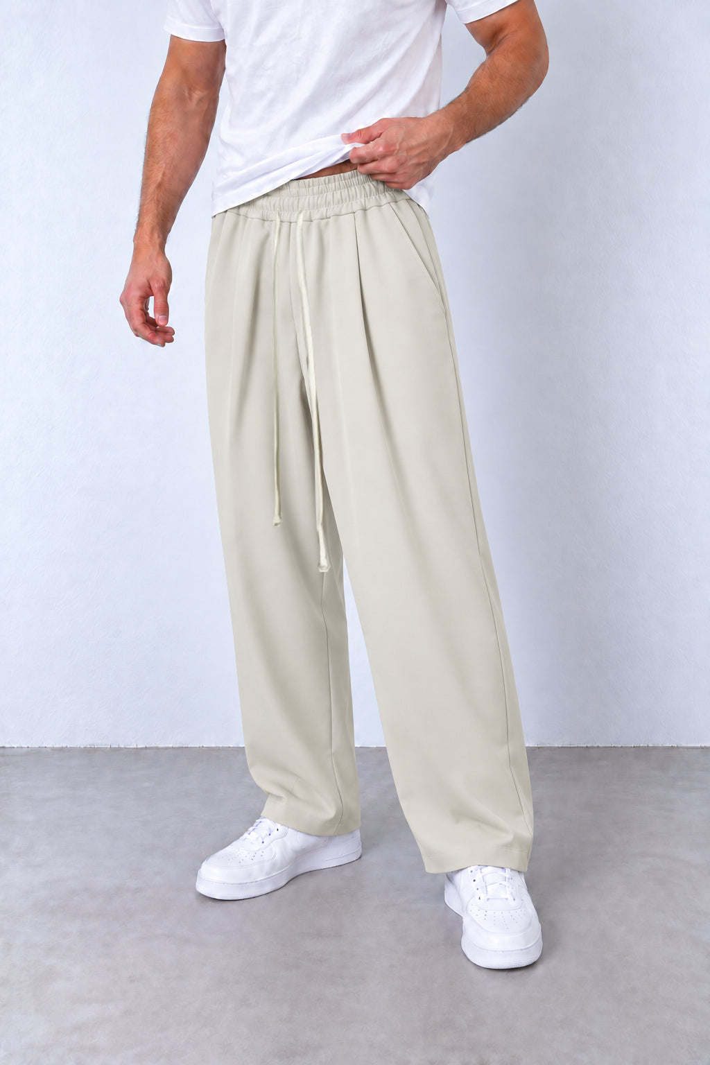 Pantaloni crem cu pense pe model, vedere din trei sferturi cu talie elastică și șnur lung.