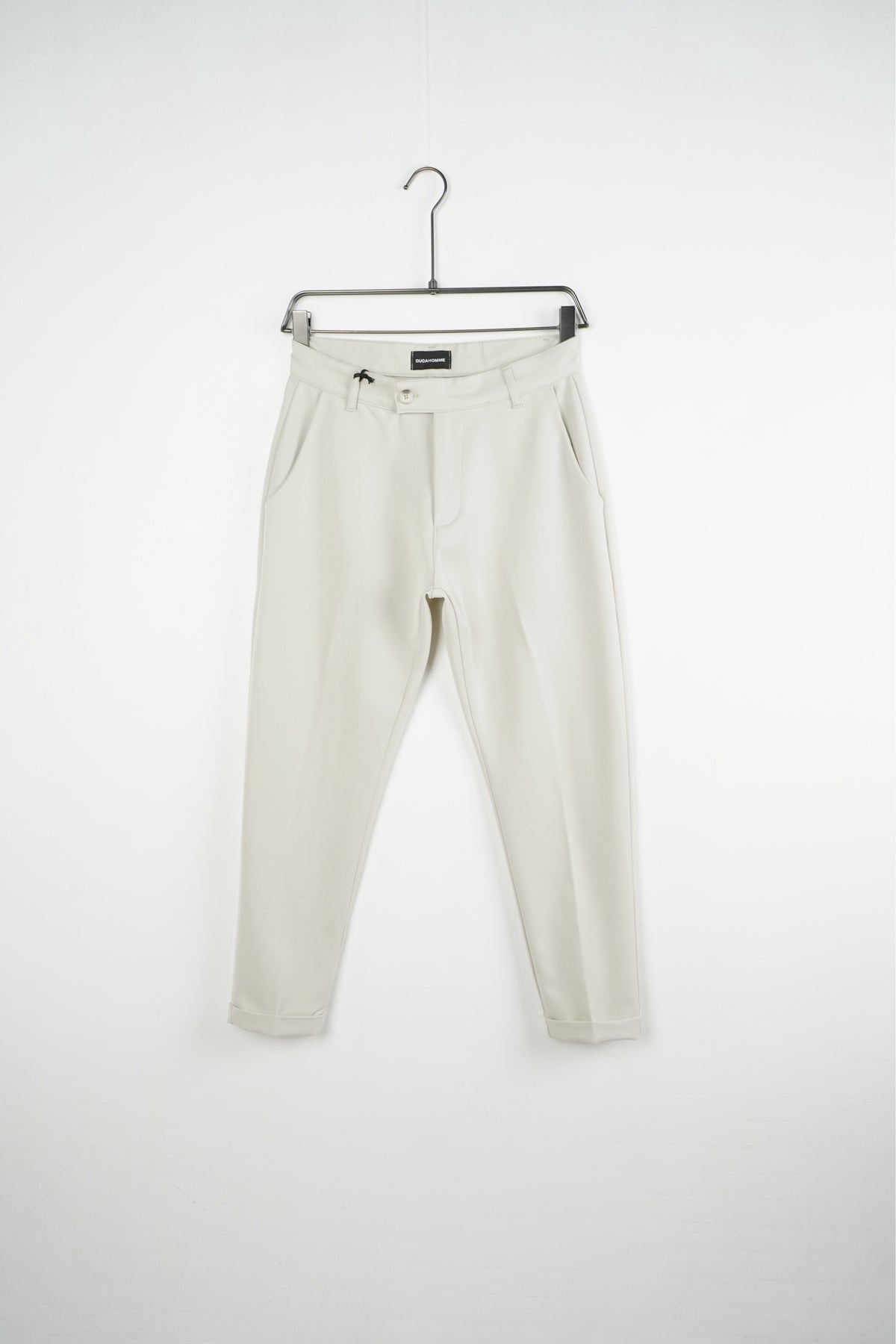 Pantaloni crem slim fit pentru bărbați, cu nasture, găici pentru curea și tiv cu rever, vedere frontală pe umeraș