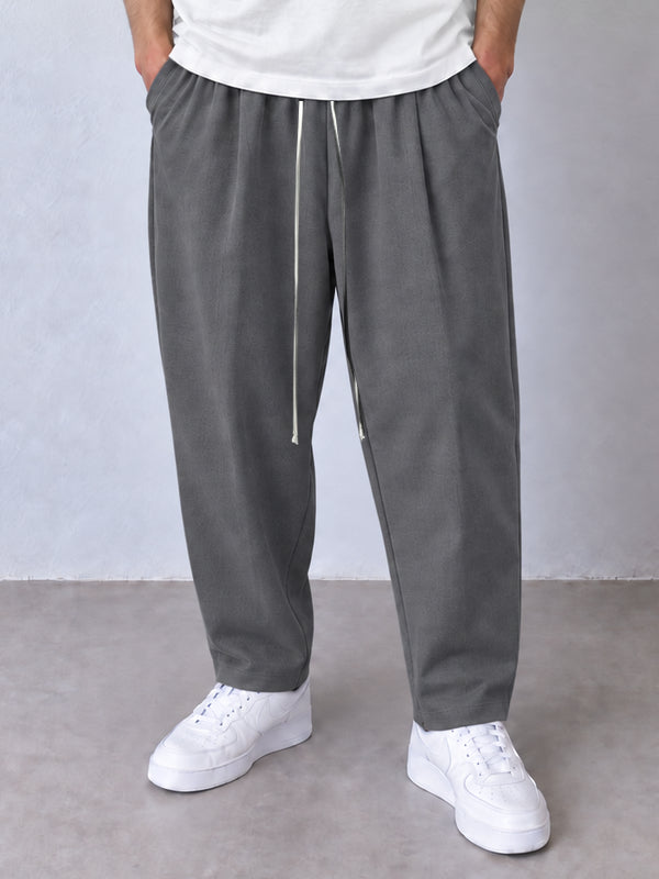 Pantaloni carrot gri, cadru frontal apropiat cu șnur lung și tiv simplu.