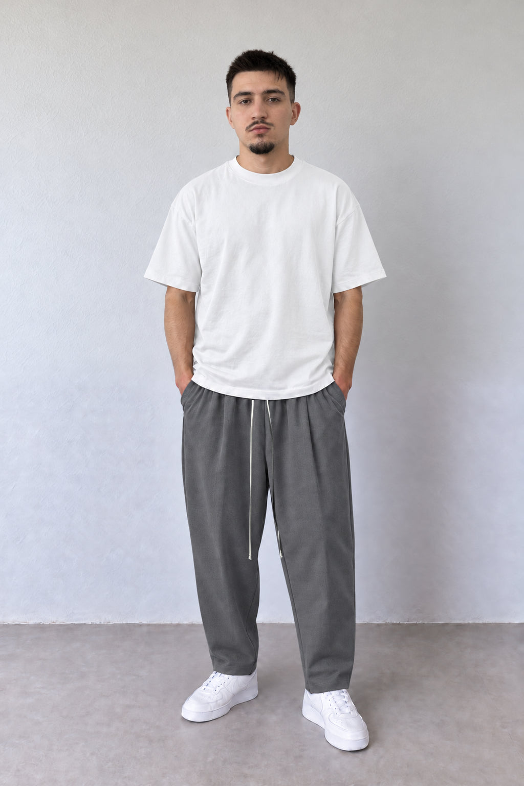 Pantaloni gri carrot fit pentru bărbați cu șnur alb lung, purtați cu tricou alb, vedere integrală.