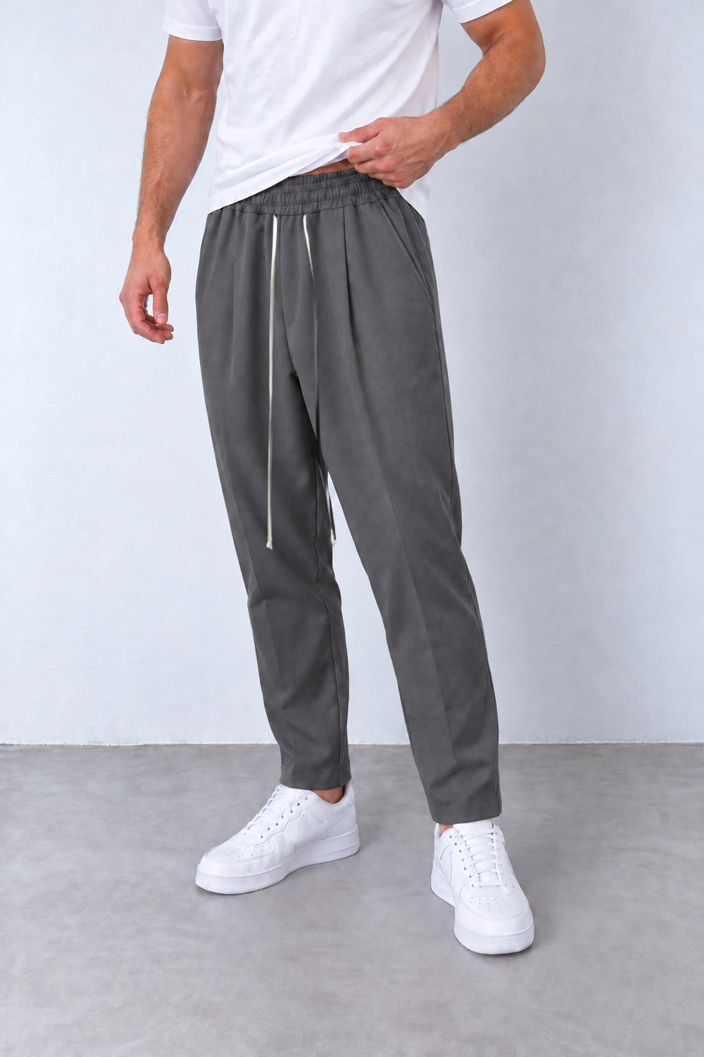 Pantaloni gri pe model, vedere din trei sferturi cu talie elastică și șnur alb lung.