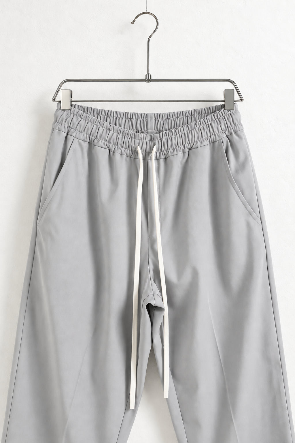 Detaliu talie elastică, buzunare și șnur lung la pantalonii gri deschis