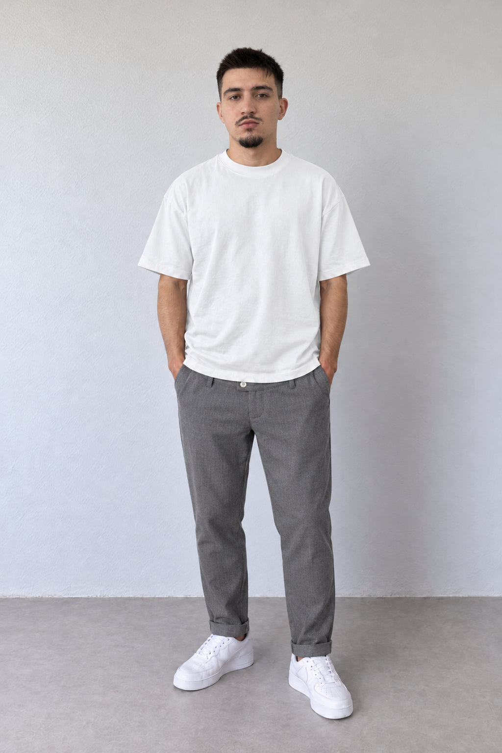 Pantaloni gri melanj slim fit pentru bărbați, cu nasture deschis la culoare și tiv cu rever, purtați cu tricou alb.