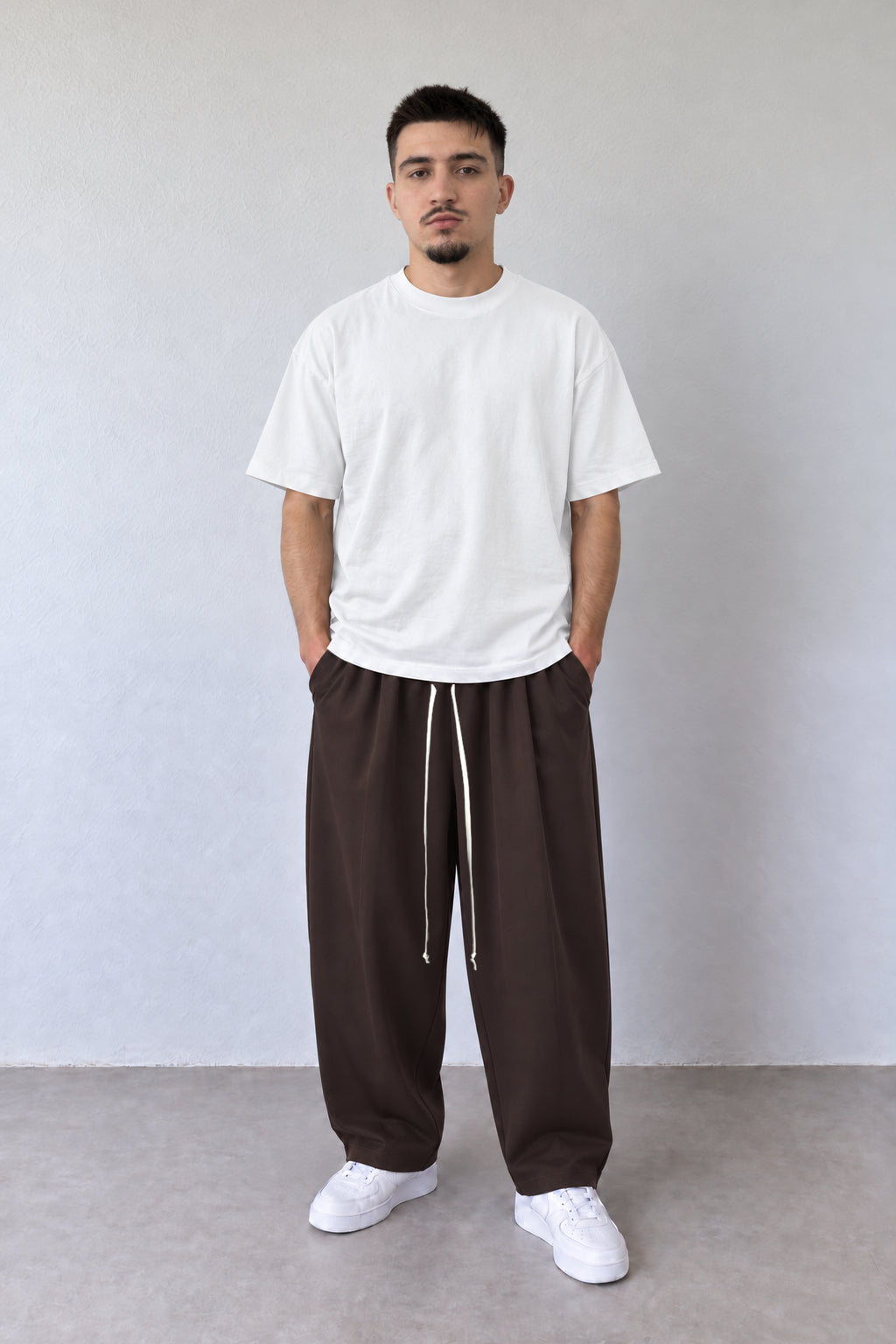 Pantaloni maro pentru bărbați cu șnur alb lung, purtați cu tricou alb, vedere integrală.