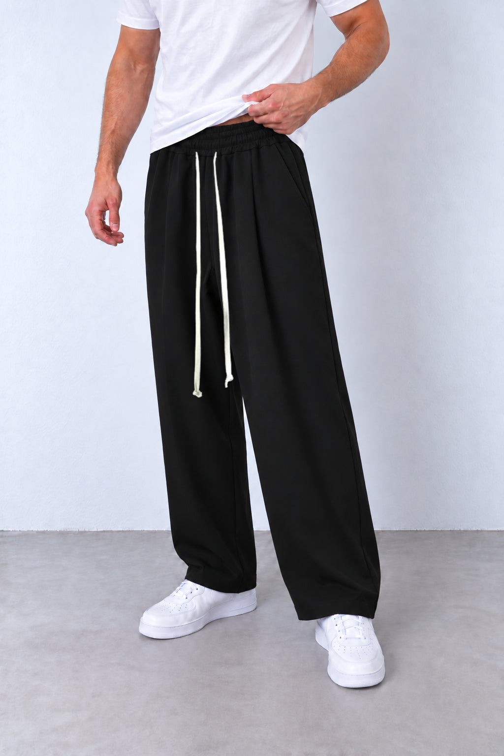 Pantaloni negri pe model, vedere din trei sferturi cu talie elastică și șnur alb lung.