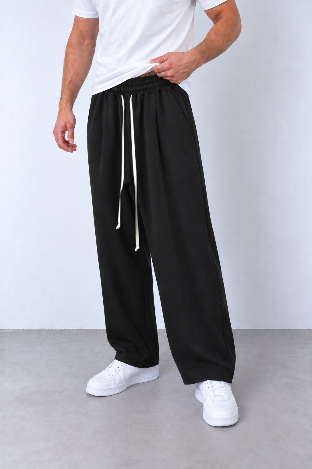 Pantaloni baggy negri, vedere din trei sferturi cu talie elastică, șnur lung și tiv simplu.