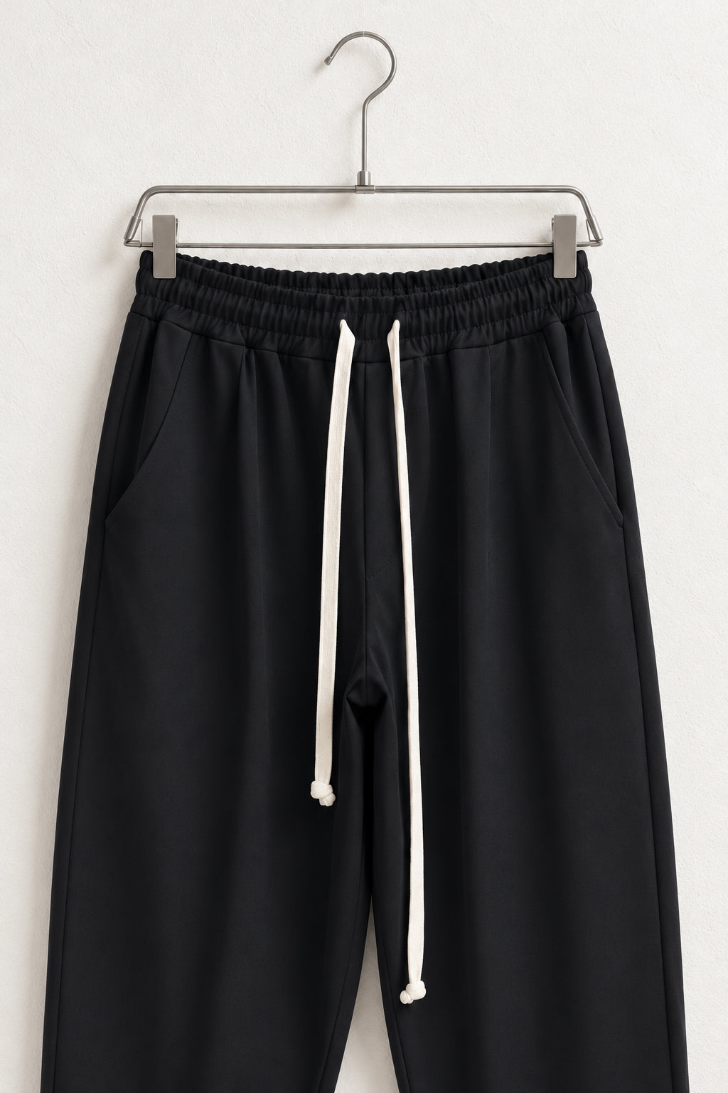 Detaliu talie elastică, buzunare și șnururi textile ale pantalonilor negri pe umeraș.
