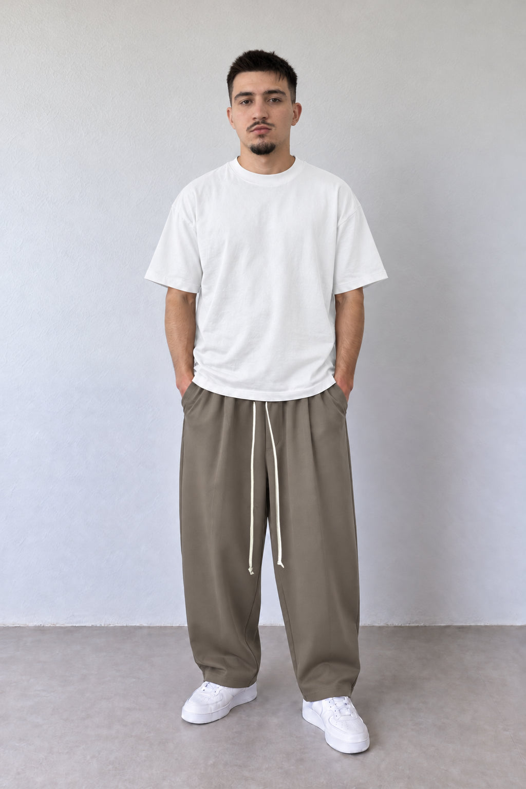 Pantaloni taupe pentru bărbați cu șnur alb lung, purtați cu tricou alb, vedere integrală.