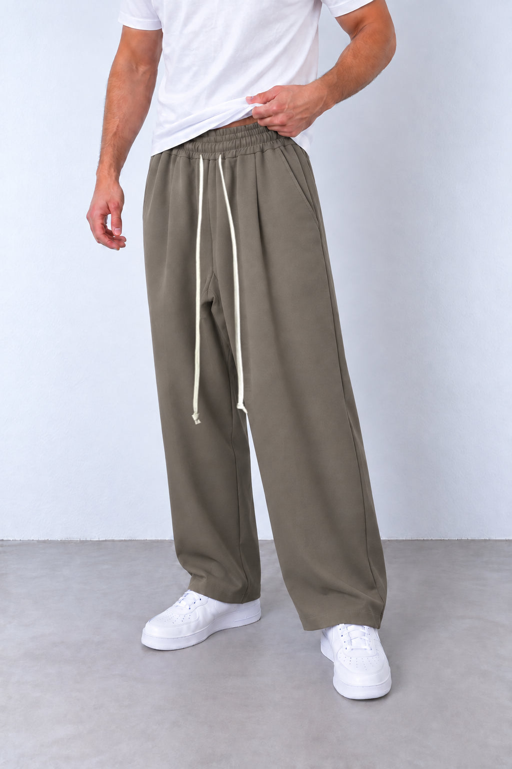 Pantaloni taupe pe model, vedere din trei sferturi cu talie elastică și șnur alb lung.