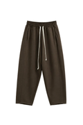 Model masculin purtând tricou alb oversized și pantaloni maro streetwear cu croială tapered, fotografiat frontal într-un stud