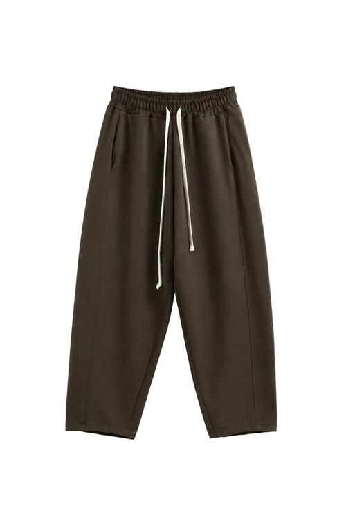 Model masculin purtând tricou alb oversized și pantaloni maro streetwear cu croială tapered, fotografiat frontal într-un stud