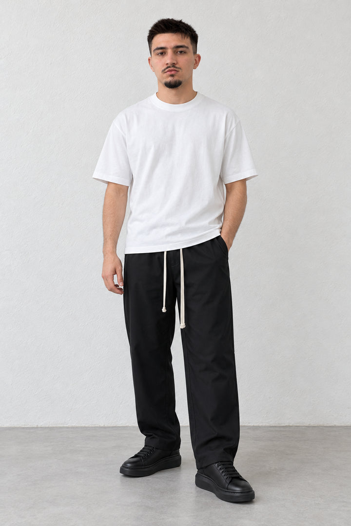Pantaloni negri cu talie elastică și tiv drept, vedere frontală pe model cu tricou alb lejer.