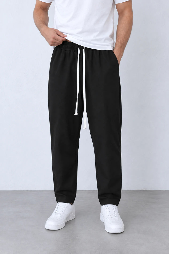 Pantaloni negri ușor slim cu talie elastică și două capete de șnur alb lung, vedere frontală apropiată.