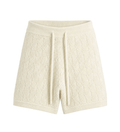 Pantaloni scurți crem, cu textură tricotată, talie elastică și șiret lung, prezentați pe un umeraș.