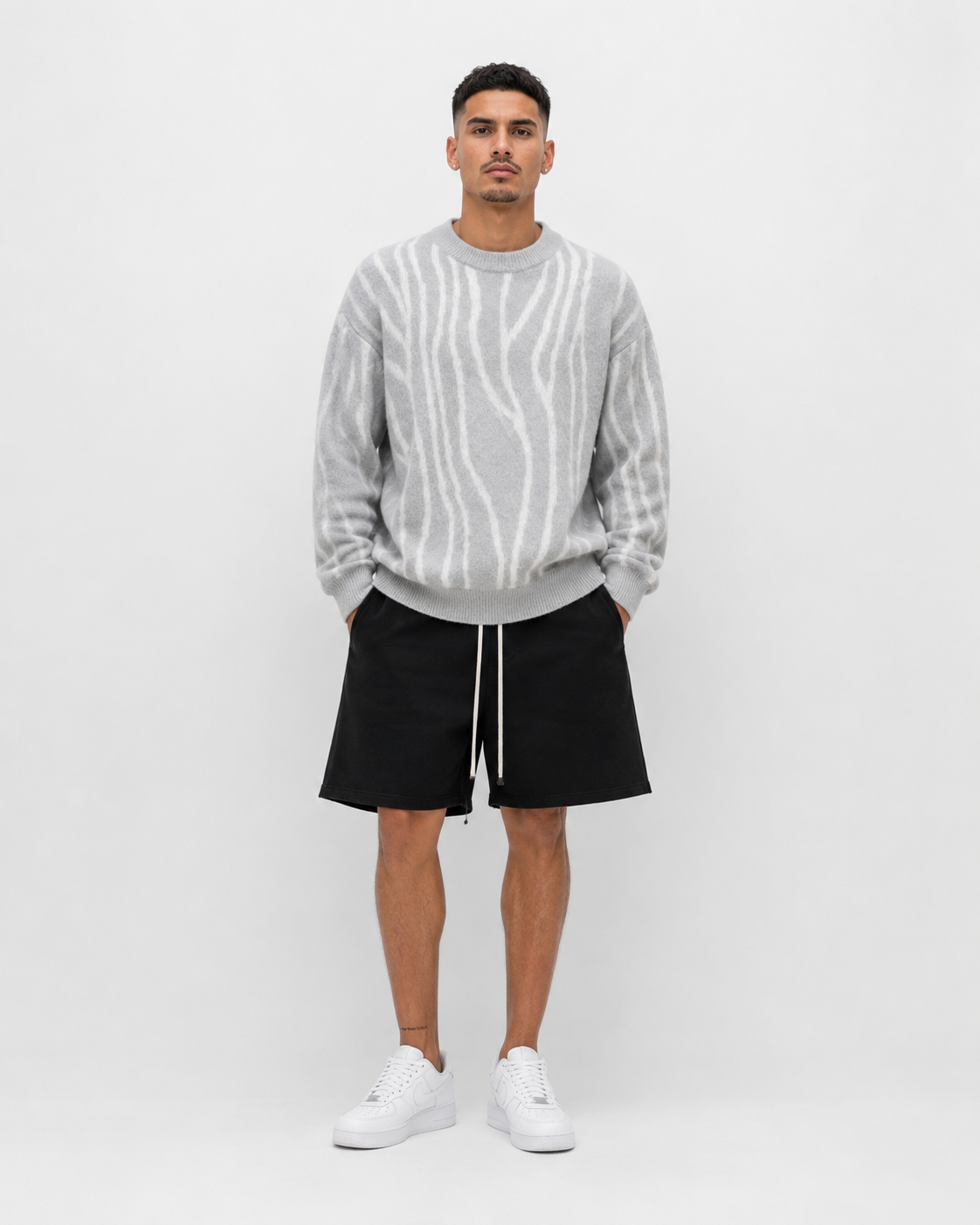 Model masculin purtând pulover oversized alb cu dungi gri, outfit luxury streetwear fotografiat în studio minimalist pe fundal alb