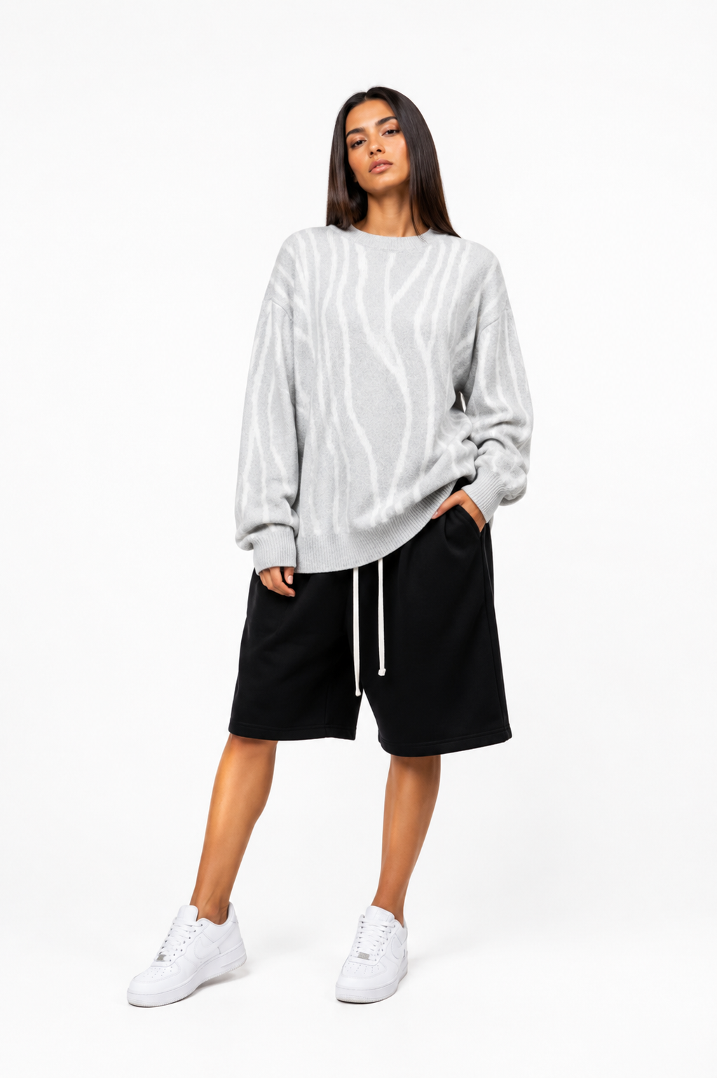 Model feminin purtând pulover oversized alb cu dungi gri în stil streetwear masculin, fotografiat în studio minimalist pe fundal alb