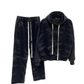 Set minimalist pentru bărbați din bumbac 100%, de culoare negru-gri cu aspect spălat, afișat pe un umeraș. Setul include un hanorac cu glugă și cusături ornamentale vizibile și pantaloni largi (wide leg) cu talie elastică și șireturi albe lungi, contrastante. Fundal perete alb texturat.